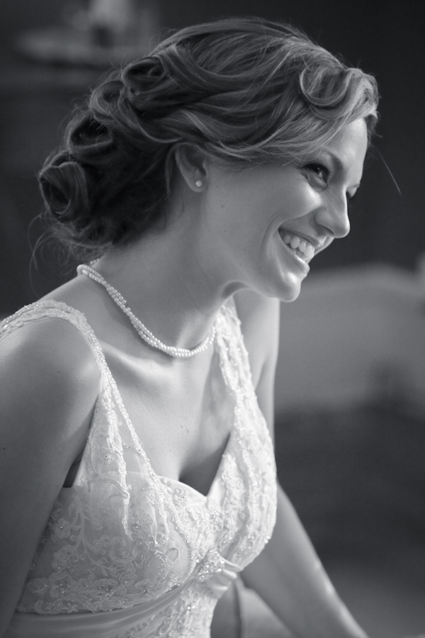 Black and white photo - Adorable photo of smiling bride - Bride is wearing white wedding dress with lace and a pearl necklace with pearl earrings - photo by North Carolina based wedding photographer Jeremie Barlow